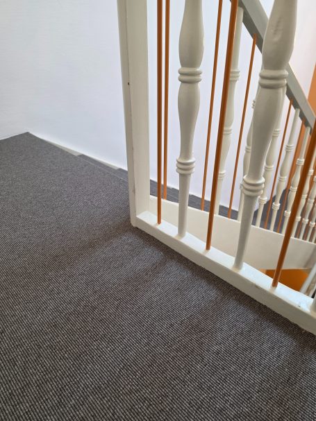 Treppenabschnitt mit Teppichboden und Geländer in hellen Farben.