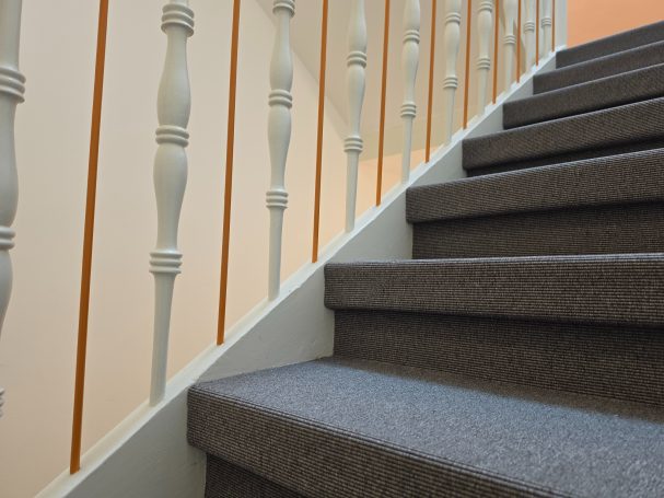 Blick auf eine Treppe mit grauem Teppichbelag und heller Geländerwand.