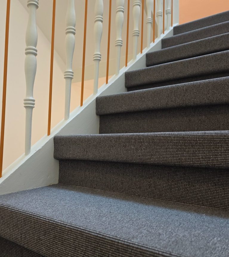 Braune Treppe mit Teppichbelag und weißen Geländerstäben.